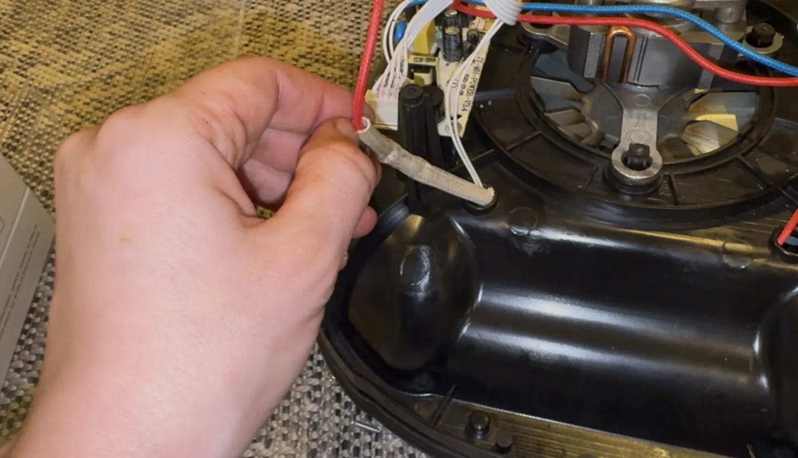 A hand holding the heat fuse wire inside the disassembled air fryer base, next to the circuit board.