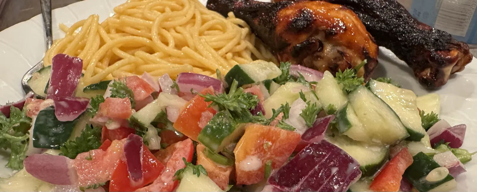A dinner plate with Brami protein pasta, grilled chicken, and a cucumber-tomato-red onion salad