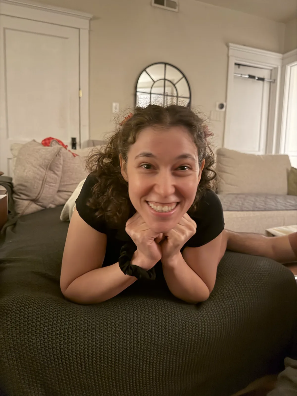 Dashiell smiling widely while leaning forward on a couch with her chin resting on her hands.