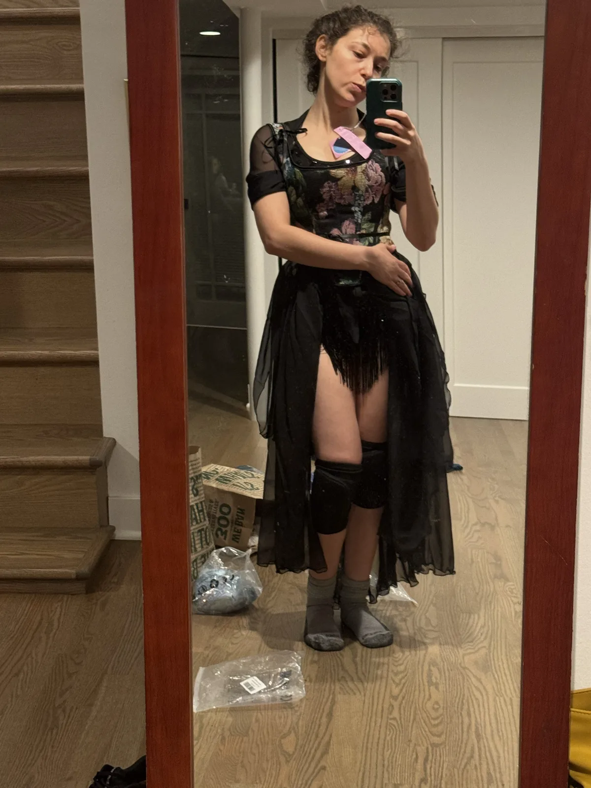 Mirror selfie wearing a floral black corset with a high-low black skirt and knee pads.