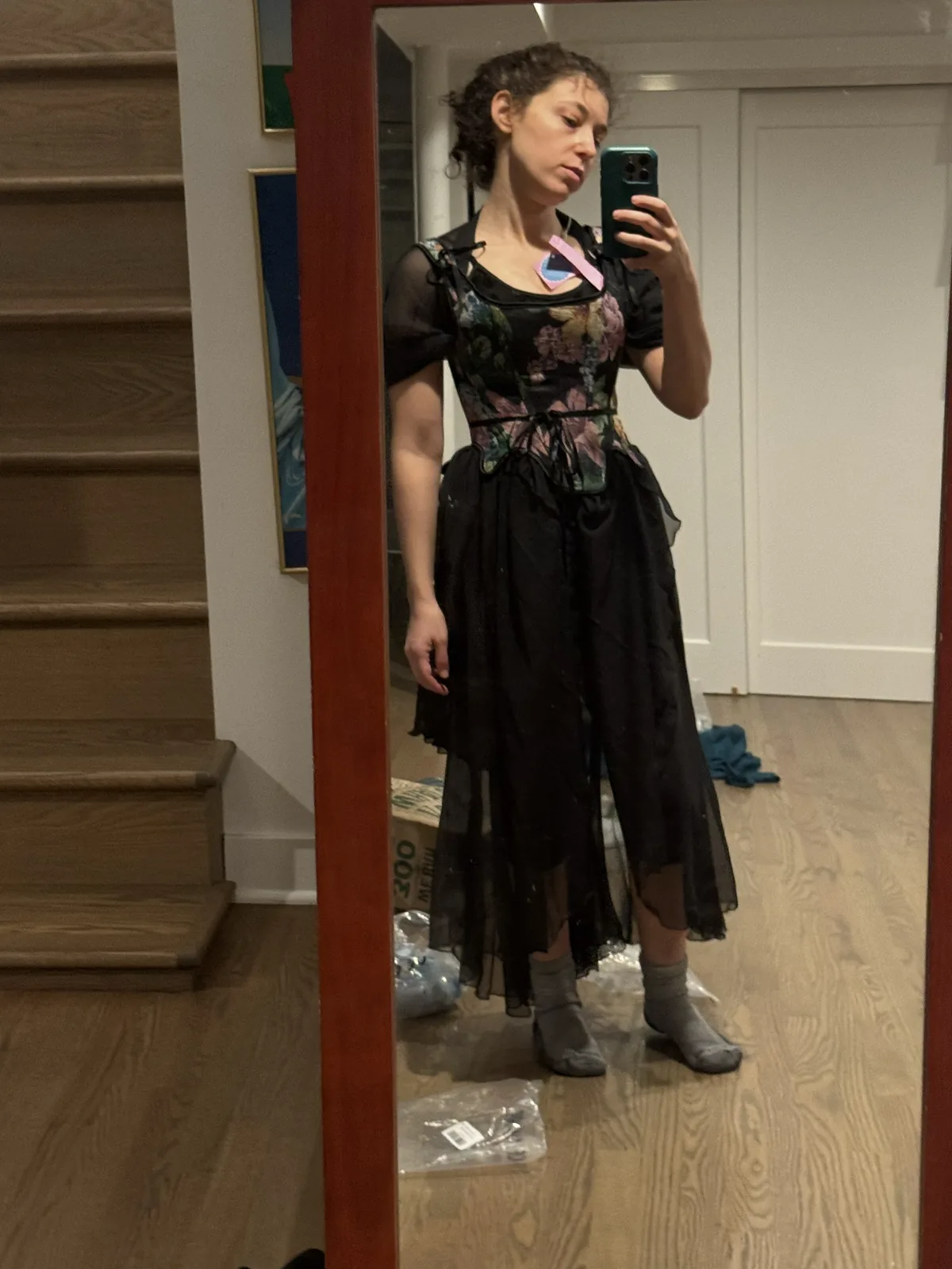 Mirror selfie wearing a floral black corset with an uneven sheer black skirt.