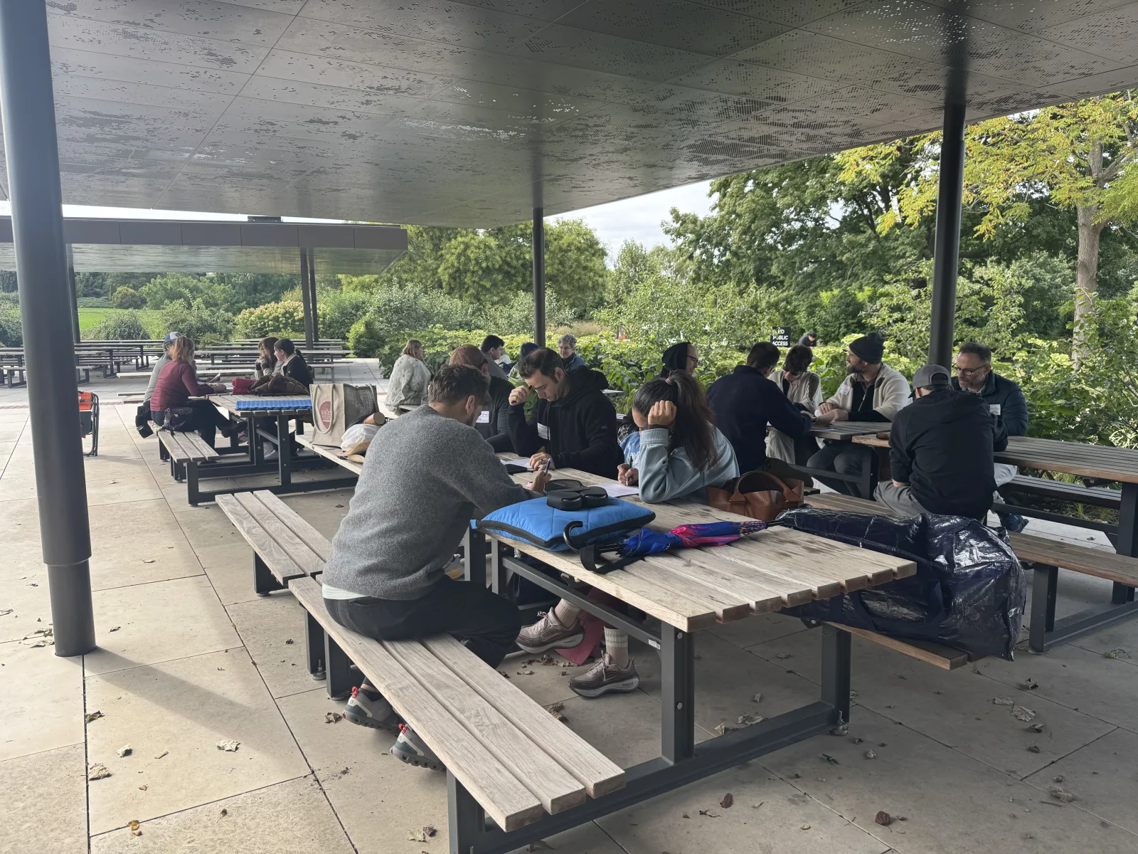 Event participants sit around picnic tables beneath a pavilion, talking and writing together.